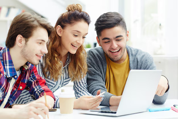 Three students smiling while using laptop